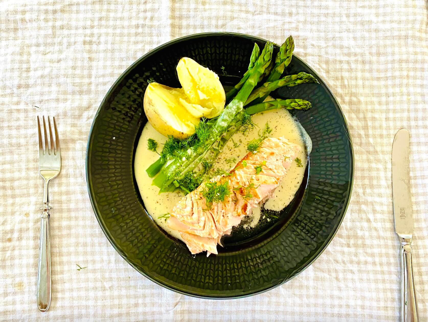 Oven baked salmon with creamy dill white wine sauce, green asparagus, and buttery Finnish new potatoes on a dinner plate
