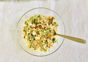 Creamy cabbage slaw with carrot, red bell pepper, leek, and parsley served in a glass bowl.