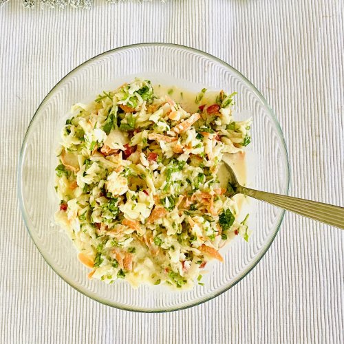 Creamy cabbage slaw with carrot, red bell pepper, leek, and parsley served in a glass bowl.
