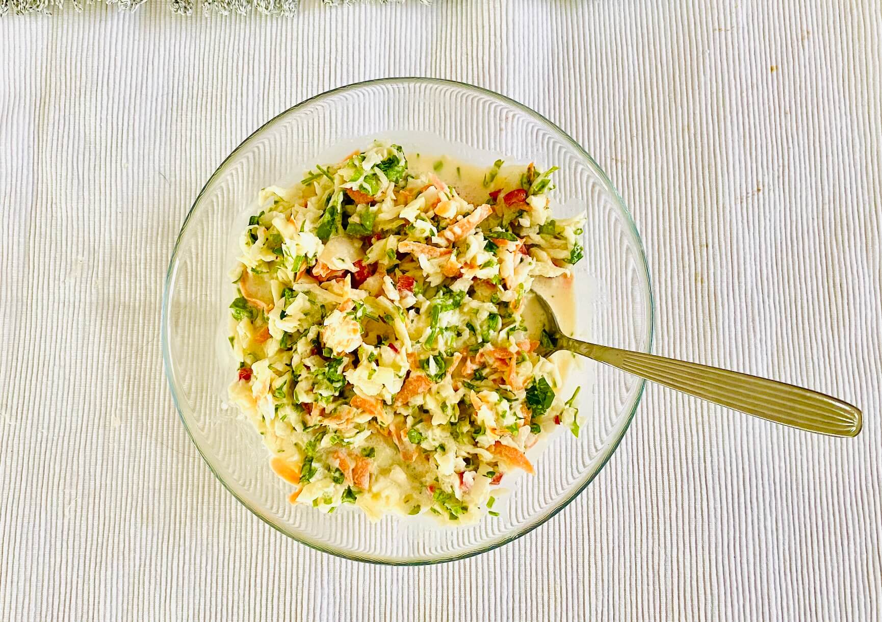 Creamy cabbage slaw with carrot, red bell pepper, leek, and parsley served in a glass bowl.