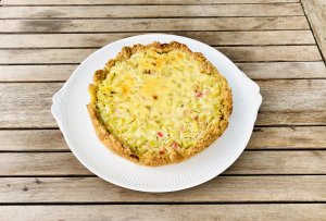 Whole Finnish rhubarb custard pie on a serving plate with a golden crust and creamy rhubarb filling.