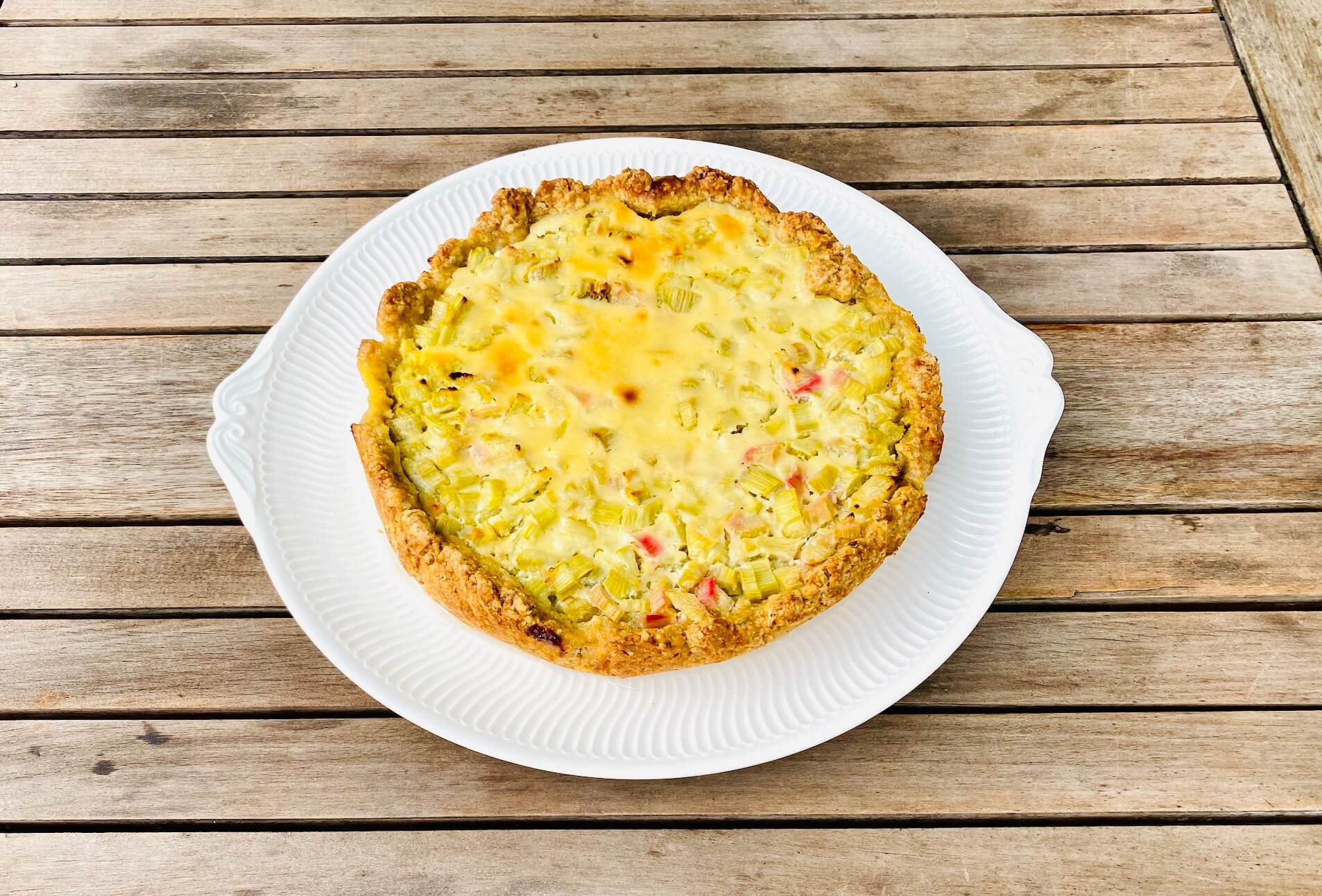 Whole Finnish rhubarb custard pie on a serving plate with a golden crust and creamy rhubarb filling.