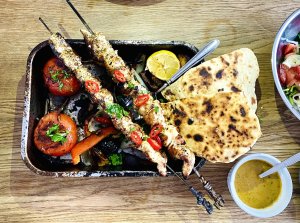 Grilled chicken skewers with roasted bell peppers, onions, and tomatoes served with smoky vegetable sauce and homemade flatbread.