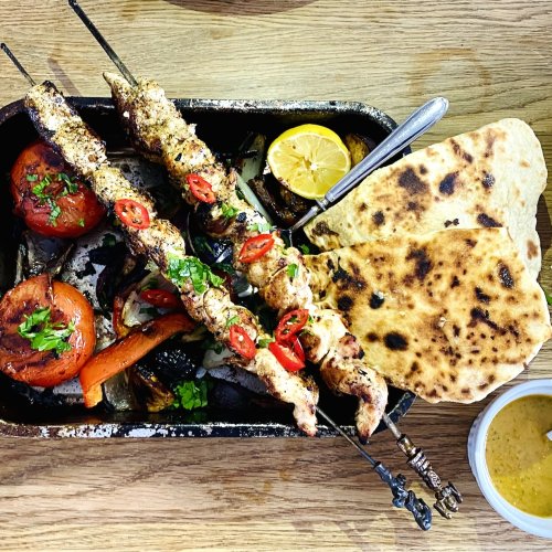 Grilled chicken skewers with roasted bell peppers, onions, and tomatoes served with smoky vegetable sauce and homemade flatbread.