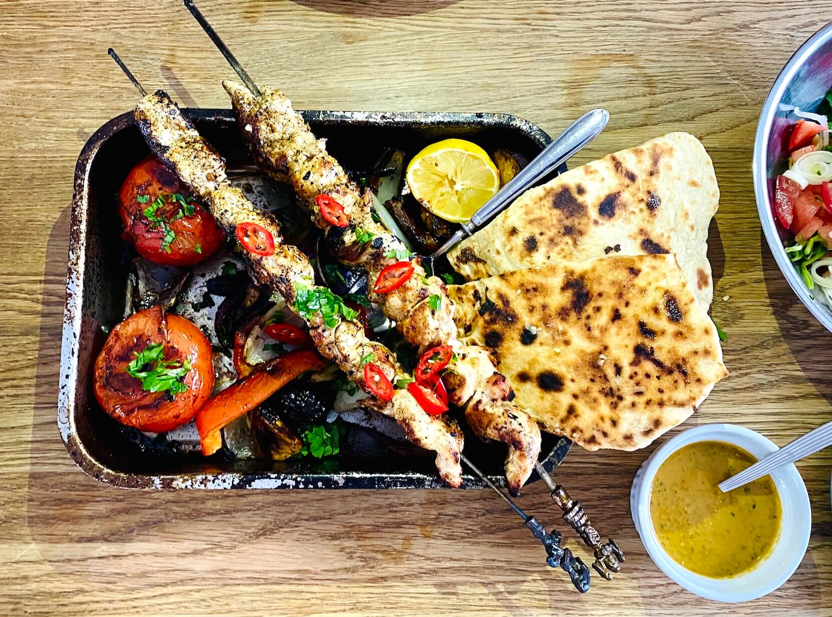 Grilled chicken skewers with roasted bell peppers, onions, and tomatoes served with smoky vegetable sauce and homemade flatbread.