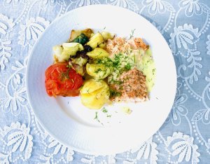 Smoked salmon with lemon dill sauce, new potatoes, and grilled vegetables on a plate.