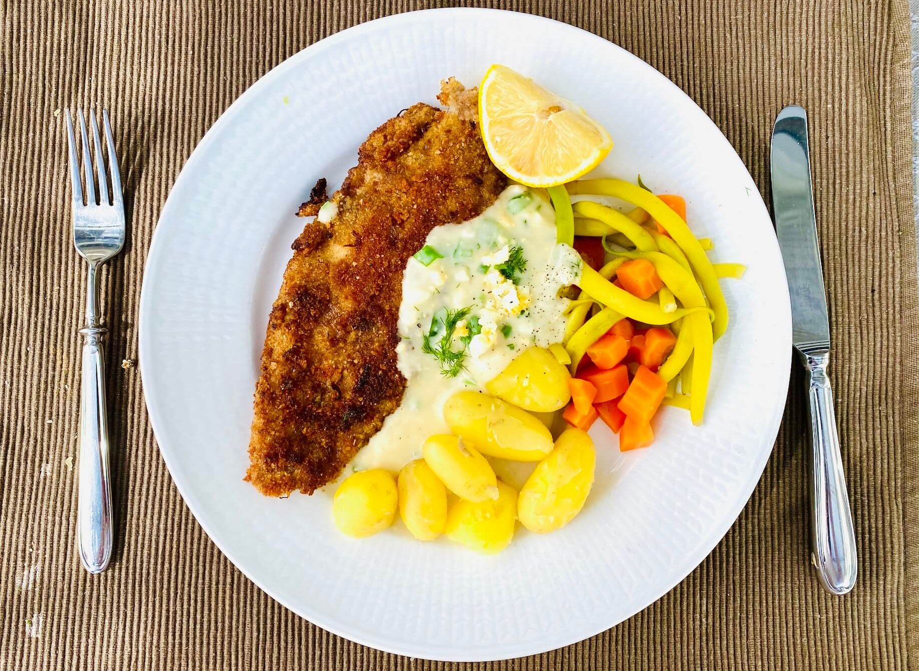 Breaded white fish served with Finnish egg sauce, new potatoes, yellow beans, and carrots