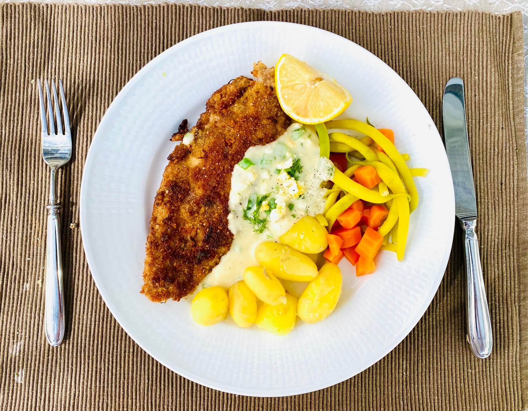 Breaded white fish served with Finnish egg sauce, new potatoes, yellow beans, and carrots