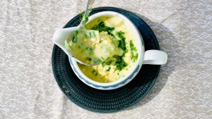 Creamy Finnish egg sauce in a gravy boat, garnished with fresh dill and chives, with the sauce pouring from a gravy ladle