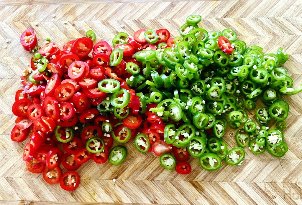 Fresh red and green chilies sliced on a wooden cutting board for Sichuan Chili Pork
