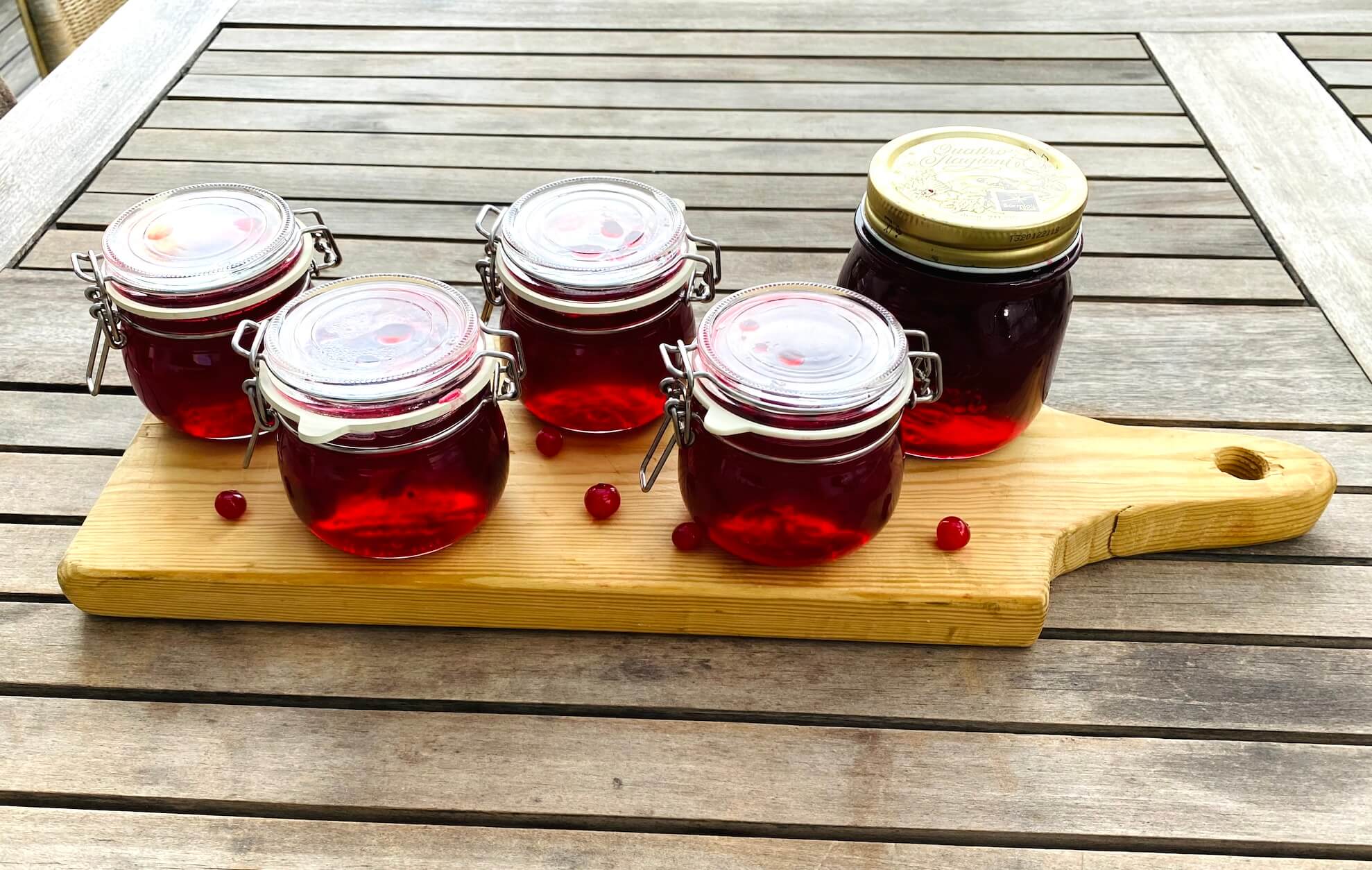 Five jars of homemade red currant jelly on a wooden board with fresh red currants