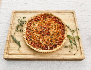 French tomato tart with sliced tomatoes and Dijon mustard on a wooden cutting board