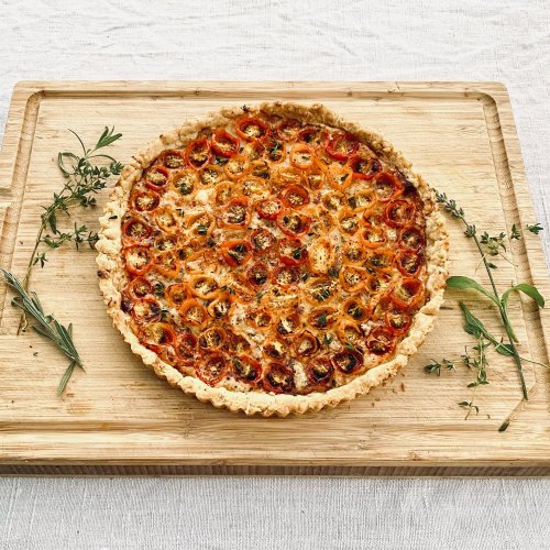 French tomato tart with sliced tomatoes and Dijon mustard on a wooden cutting board