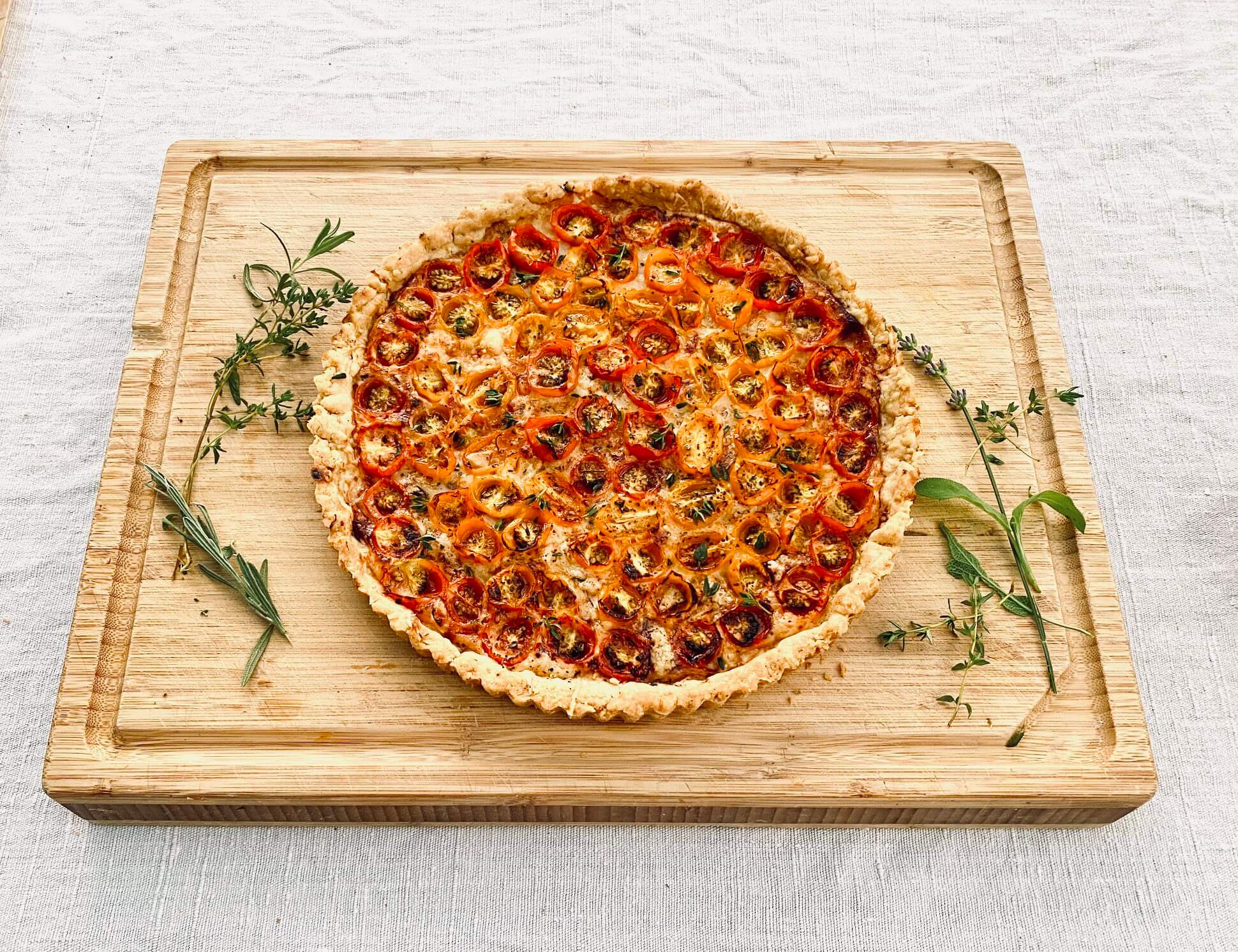 French tomato tart with sliced tomatoes and Dijon mustard on a wooden cutting board