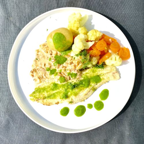 Pan-fried white fish fillet with dill oil, new potatoes, cauliflower, carrots, and chanterelle sauce on a plate.