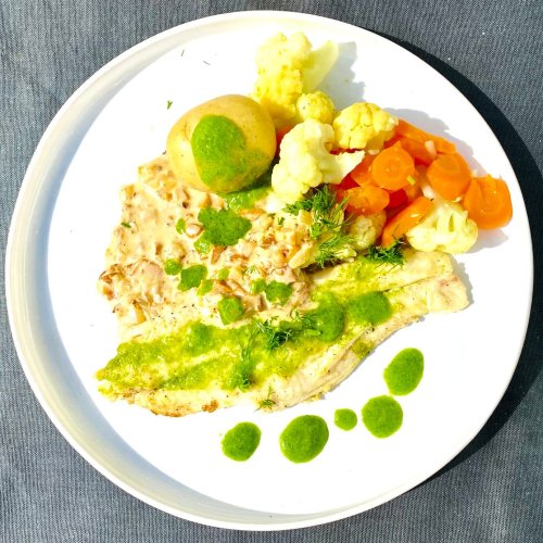 Pan-fried white fish fillet with dill oil, new potatoes, cauliflower, carrots, and chanterelle sauce on a plate.