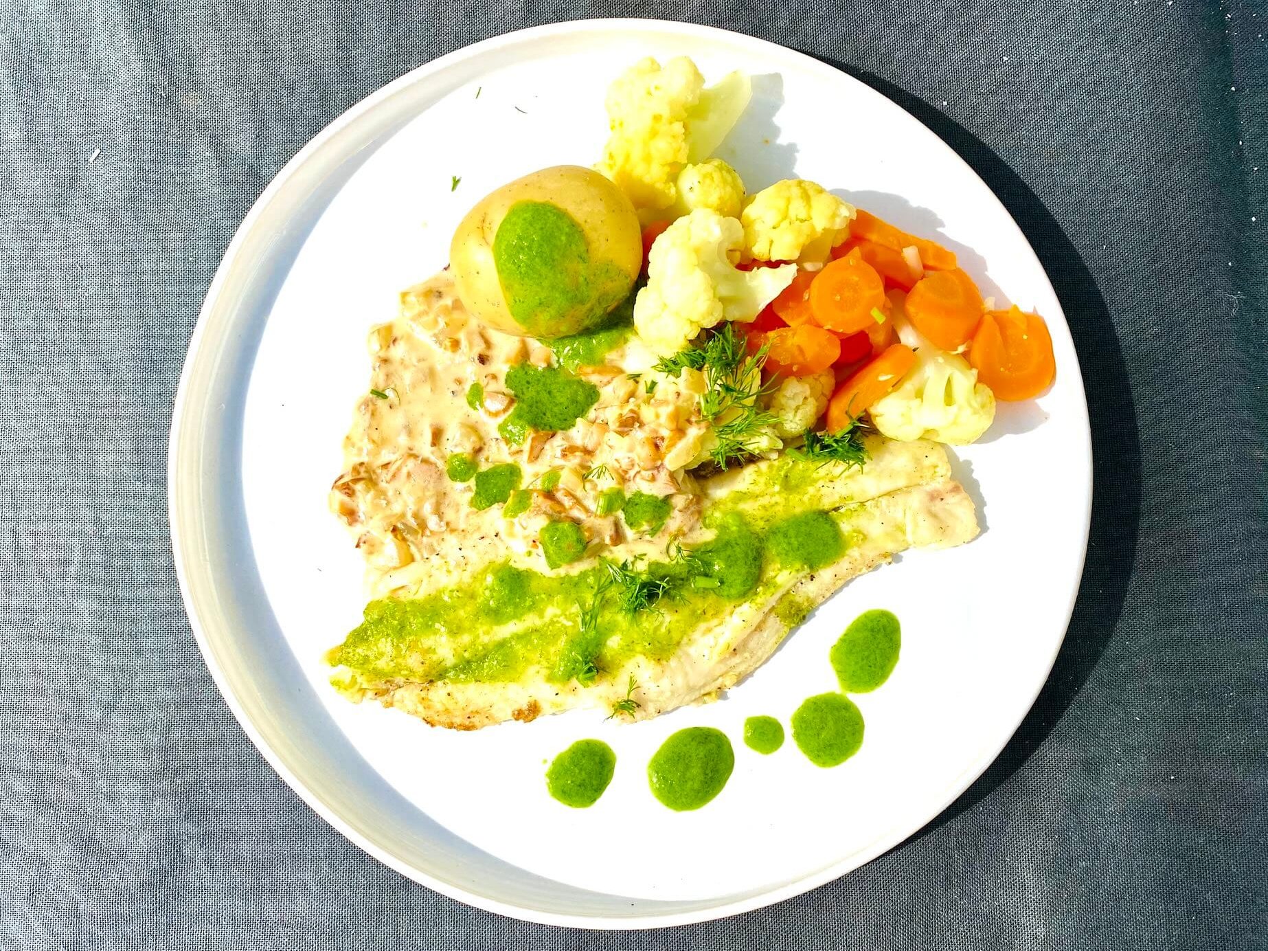 Pan-fried white fish fillet with dill oil, new potatoes, cauliflower, carrots, and chanterelle sauce on a plate.