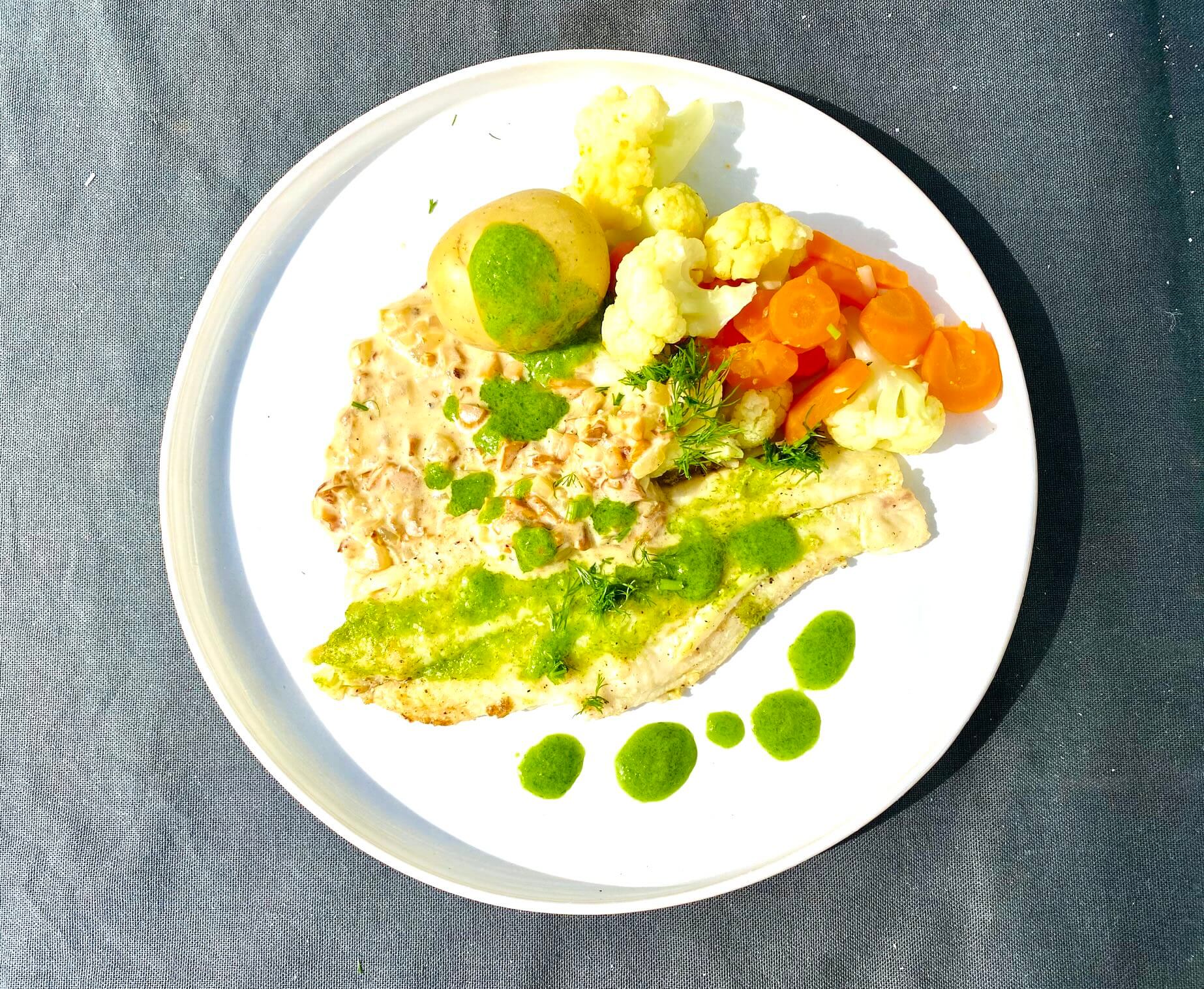 Pan-fried white fish fillet with dill oil, new potatoes, cauliflower, carrots, and chanterelle sauce on a plate.