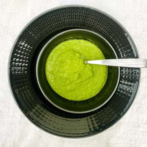 Creamy pea puree made with frozen peas, onion, vegetable stock, and cream, served in a dark grey bowl.