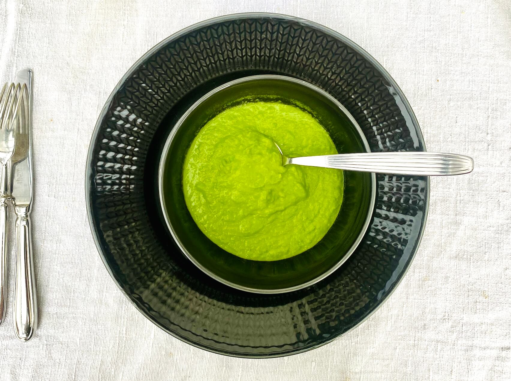 Creamy pea puree made with frozen peas, onion, vegetable stock, and cream, served in a dark grey bowl.