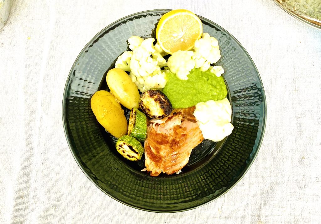 Grilled salmon served with creamy pea puree, Finnish new potatoes, grilled zucchini, cauliflower, and horseradish sauce on a dinner plate.