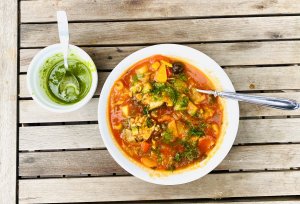 Tomato-based salmon and white fish soup with potatoes and vegetables, topped with dill oil and served with extra dill oil on the side.