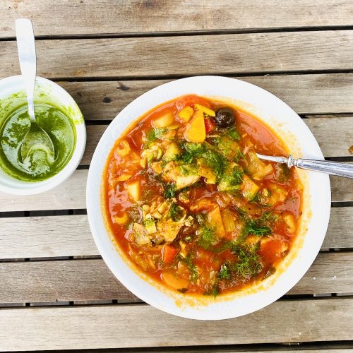 Tomato-based salmon and white fish soup with potatoes and vegetables, topped with dill oil and served with extra dill oil on the side.