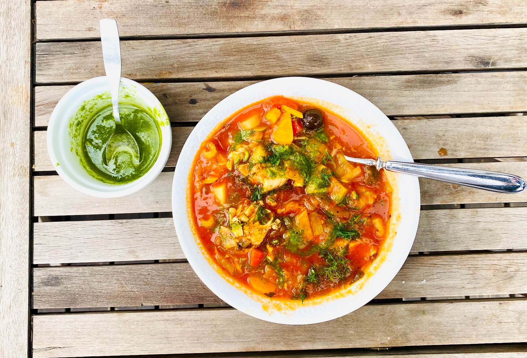 Tomato-based salmon and white fish soup with potatoes and vegetables, topped with dill oil and served with extra dill oil on the side.