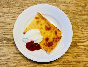 Slice of Finnish oven pancake with raspberry jam and whipped cream on a plate