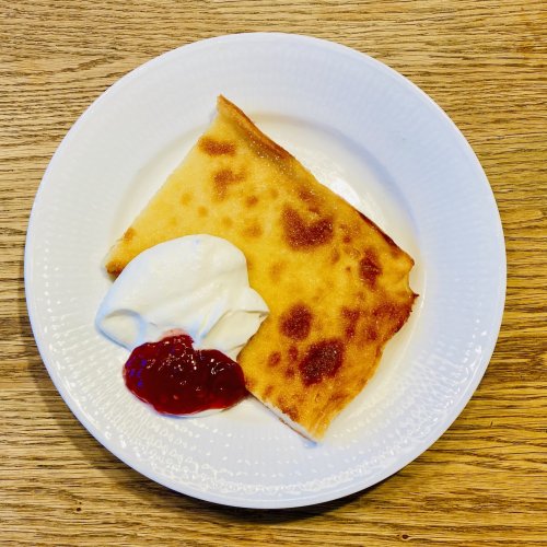 Slice of Finnish oven pancake with raspberry jam and whipped cream on a plate