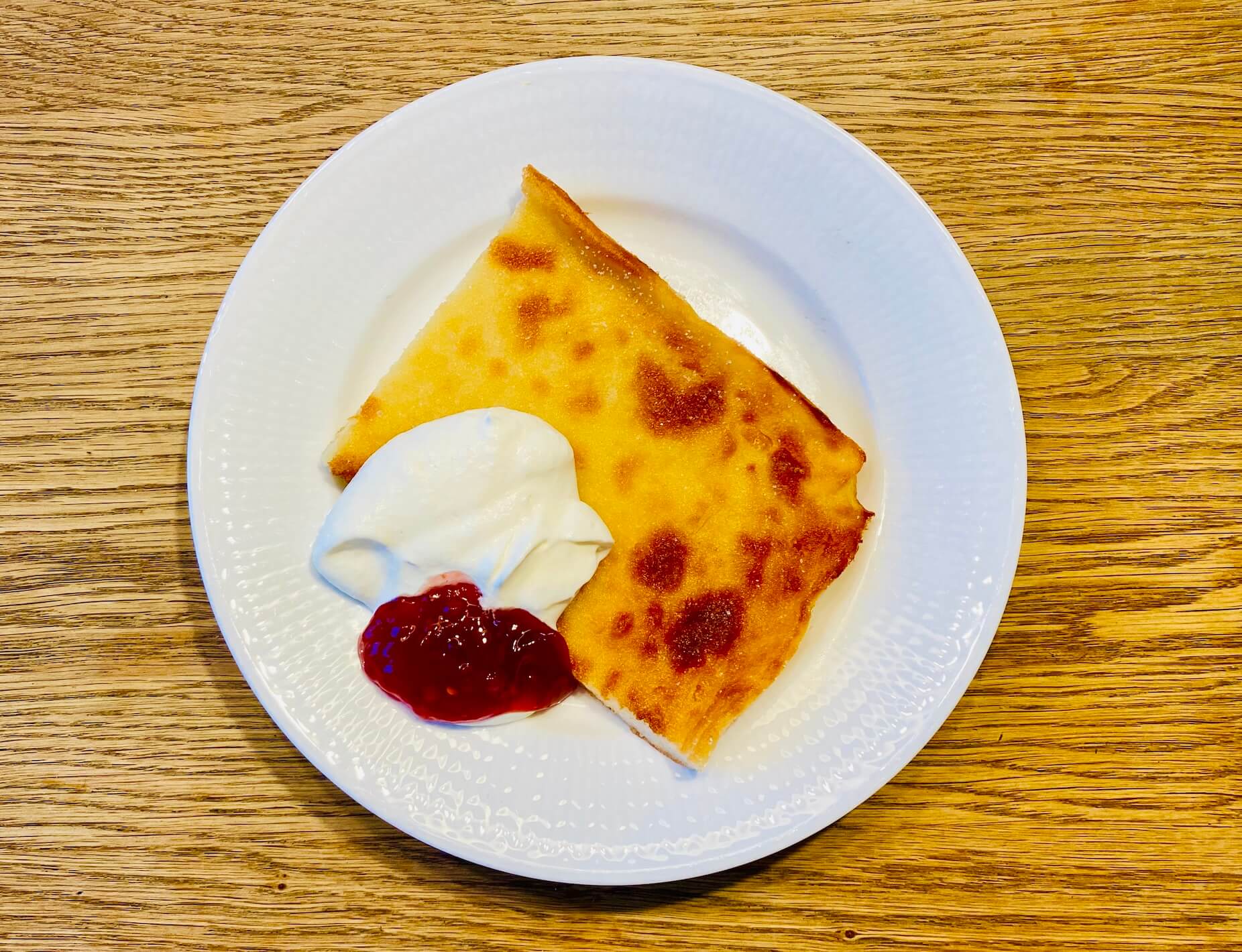 Slice of Finnish oven pancake with raspberry jam and whipped cream on a plate