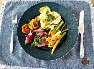 Sliced roast beef with red wine pan sauce, vegetables, roasted tomatoes, creamy garlic potatoes, and red currant jelly