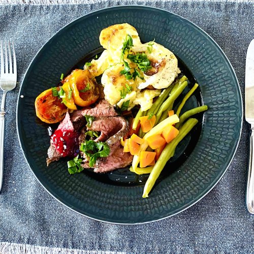 Sliced roast beef with red wine pan sauce, vegetables, roasted tomatoes, creamy garlic potatoes, and red currant jelly