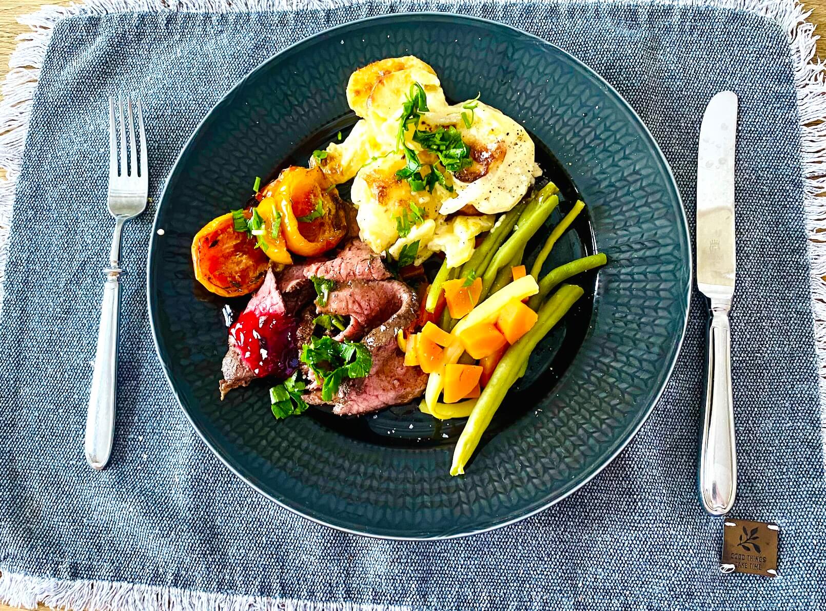 Sliced roast beef with red wine pan sauce, vegetables, roasted tomatoes, creamy garlic potatoes, and red currant jelly