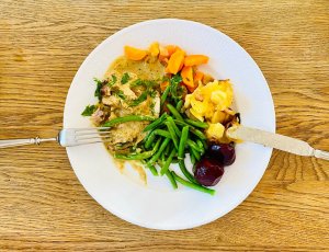 Sliced roast pork with creamy parsley sauce, garlic potatoes, green beans, carrots, and pickled beetroot on a plate.