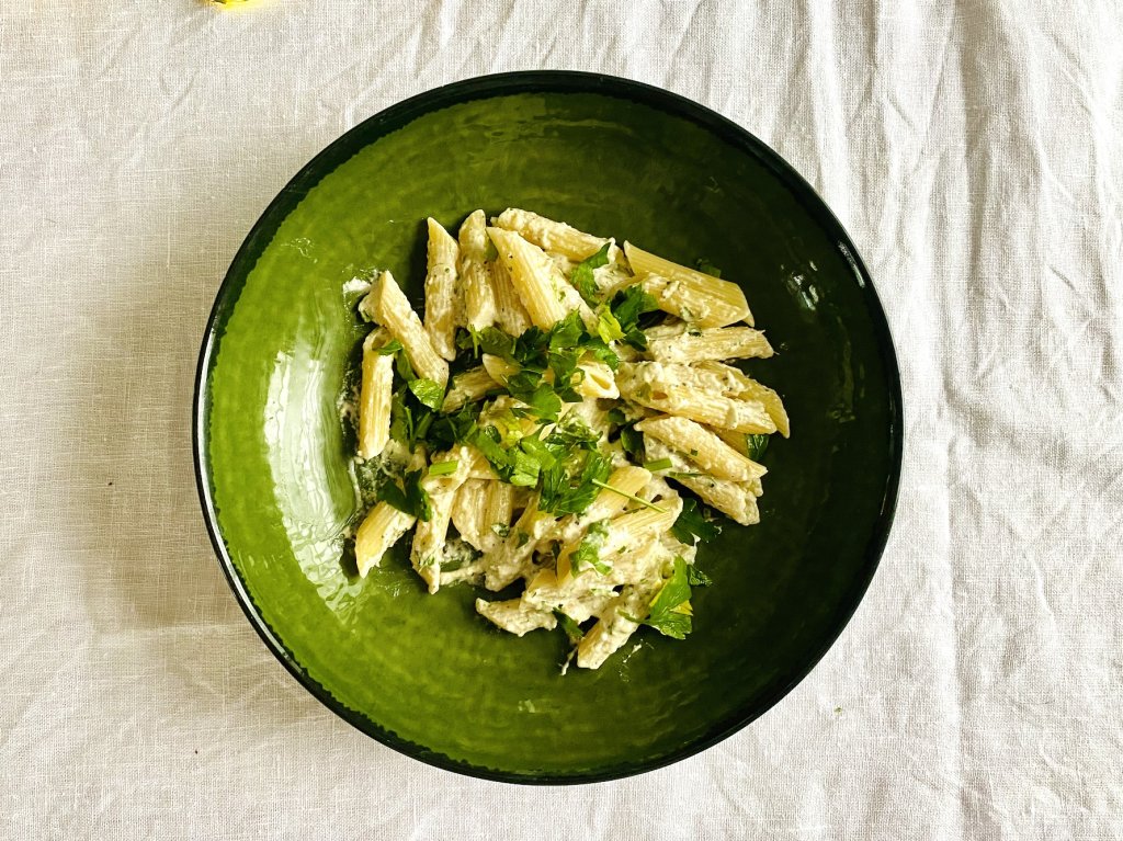 Penne pasta tossed with white pesto and garnished with chopped fresh parsley in a green bowl.