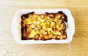 Oven-baked garlic potatoes in a baking dish, with thinly sliced potatoes and a lightly browned, crispy top layer.