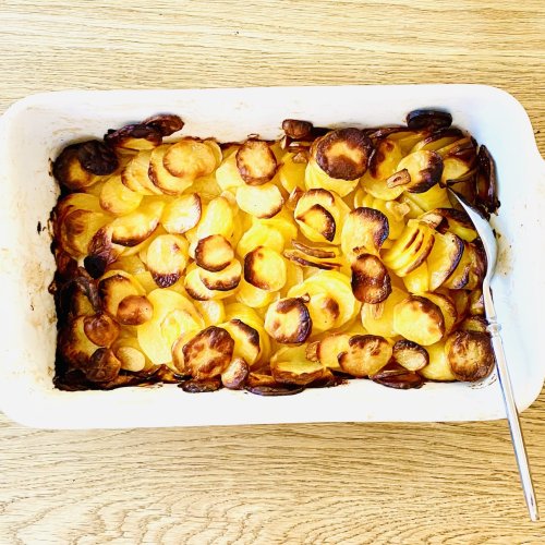 Oven-baked garlic potatoes in a baking dish, with thinly sliced potatoes and a lightly browned, crispy top layer.