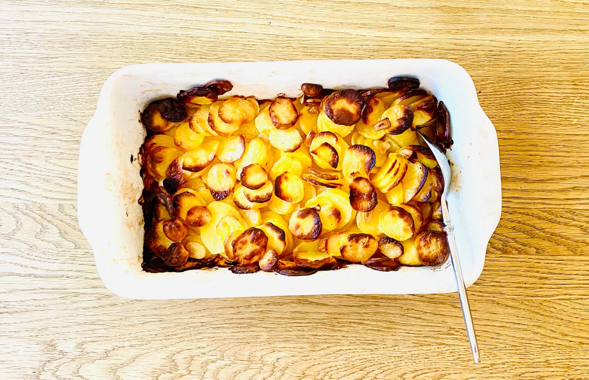 Oven-baked garlic potatoes in a baking dish, with thinly sliced potatoes and a lightly browned, crispy top layer.